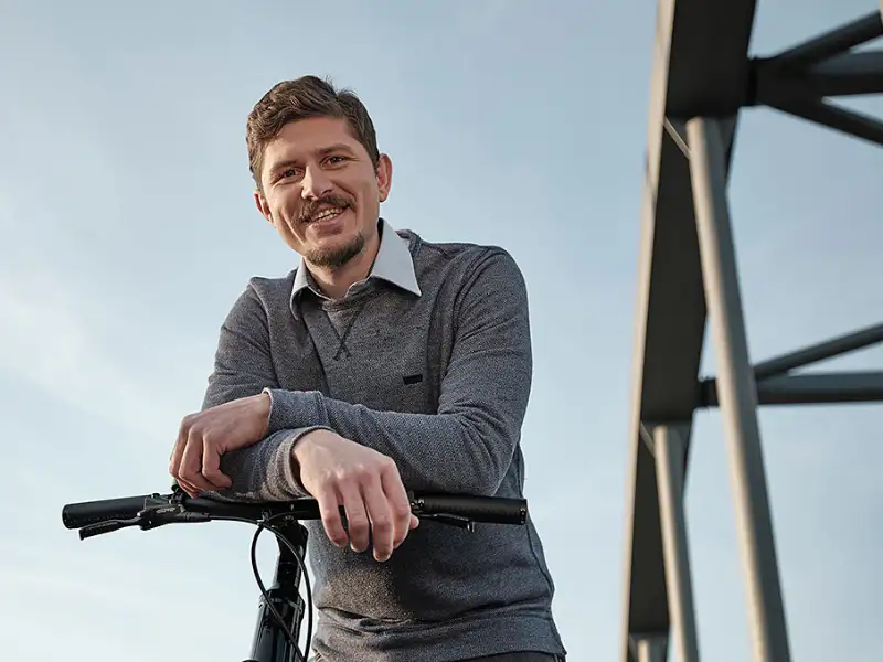 Ein lächelnder Mann auf einer Brücke lehnt über seinem Fahrradlenker Ein lächelnder Mann auf einer Brücke lehnt über seinem Fahrradlenker